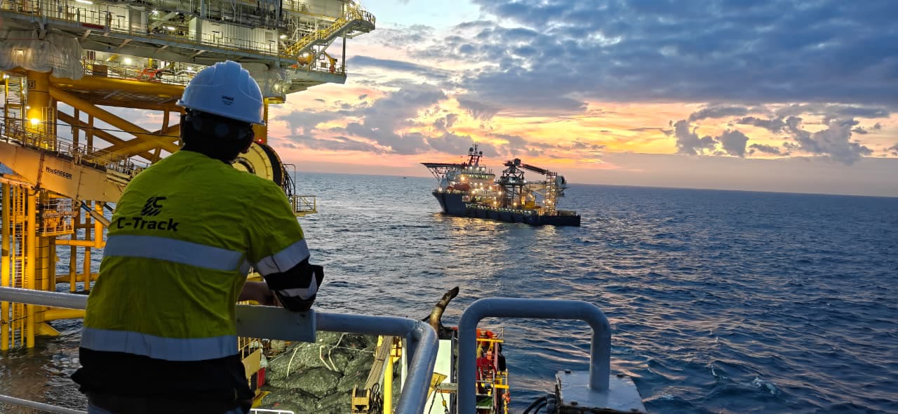 C-TRACK surveyor watching a construction vessel beside an offshore platform at sunset
